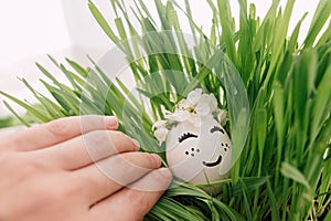 Happy Easter and Easter hunt! Hand holding egg with sleeping face in floral wreath in green grass