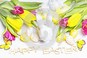 Happy Easter. Easter white bunny on a white background with Easter eggs and fresh tulips.Easter greeting card with easter bunny.