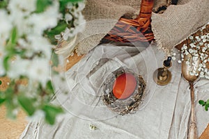 Happy Easter flat lay. Modern Easter egg in nest on rustic table with spring flowers, candle,basket. Stylish red Easter egg