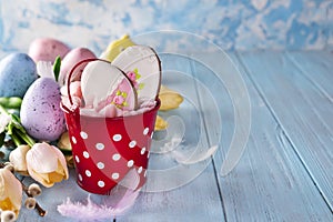 Happy Easter gingerbread cookie eggs with bucket and tulips with colorful eggs on blue wood background,