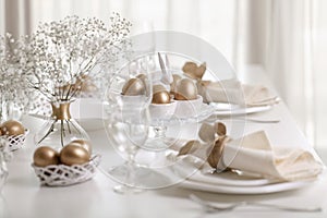 Happy Easter! Golden decor and table setting of the Easter table with white dishes of white color