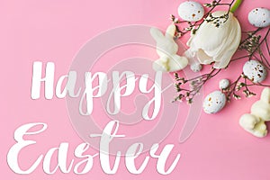 Happy Easter greeting card. Happy Easter text and modern eggs, tulips, bunnies flat lay on pink background. Seasons greeting card