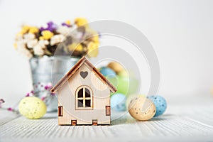 Happy Easter greeting card. Miniature wooden house. Rabbits, colorful eggs, spring flowers with tag for text..