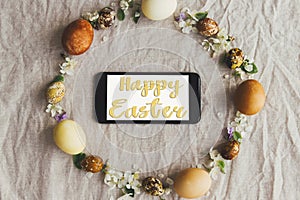 Happy Easter greeting card. Happy Easter text sign handwritten on  phone screen in easter rustic wreath with eggs and flowers flat
