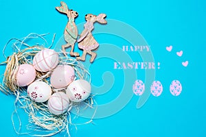 Happy Easter greeting card. Top view of colorful eggs with straw and a couple of wooden easter bunnies flat lay on a blue