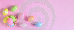 Happy Easter holiday greeting card concept. Colorful Easter Eggs and spring flowers on pastel pink background. Flat lay, top view