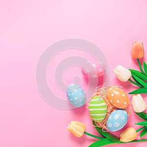 Happy Easter holiday greeting card concept. Colorful Easter Eggs and spring flowers on pastel pink background. Flat lay, top view