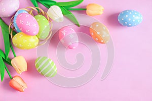 Happy Easter holiday greeting card concept. Colorful Easter Eggs and spring flowers on pastel pink background. Flat lay, top view