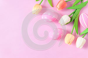 Happy Easter holiday greeting card concept. Colorful Easter Eggs and spring flowers on pastel pink background. Flat lay, top view