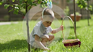 Happy easter holiday little kid boy pick up easter egg in grass put in basket