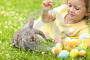 Happy Easter kid. little girl with very peri ears, small rabbit, grey bunny hunting for colorful eggs on green grass