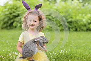 Happy Easter kid. little girl with very peri ears, small rabbit, grey bunny hunting for colorful eggs on green grass. spring holid