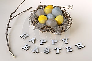 Happy easter lettering, branch and colorful Easter eggs in birds nest on gray background