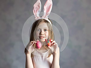 Happy Easter. A little girl with blond hair holds Easter eggs in her hands, rejoices, smiles