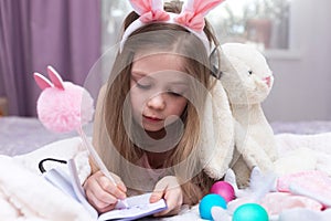 happy Easter. A little girl with blonde hair is lying on a bed with a toy rabbit