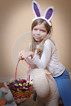 Happy Easter! Little girl rides a fluffy bunny with a spring flowers in a basket