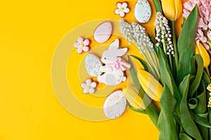 Happy Easter. Multi-colored pastel easter cookies gingerbread, seasonal flowers tulips on bright yellow background. Easter concept