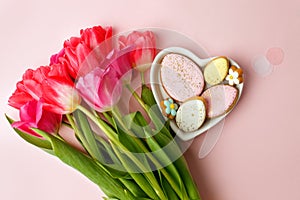 Happy Easter. Multi-colored pastel easter cookies gingerbread, seasonal flowers tulips on pink background. Easter concept, copy