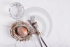 Happy easter naturally colored egg in nest, cutlery and glass of water on table top view