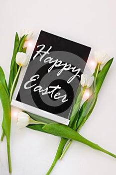 Happy Easter sample text on black chalkboard with tulip flowers on white background. Natural floral spring decorations