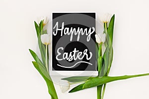 Happy Easter sample text on black chalkboard with tulip flowers on white background. Natural floral spring decorations
