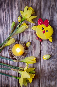 Happy Easter. Spring flowers yellow daffodils, easter eggs, candle and gingerbread chicken on a wooden background. Top view