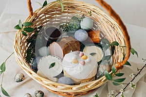 Happy Easter! Stylish easter basket with natural dyed eggs, meat, bread, butter, beets and spring flowers on rustic table.