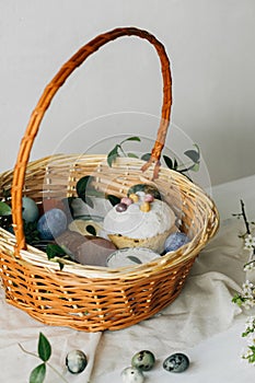 Happy Easter! Stylish easter basket with natural dyed eggs, meat, bread, butter, beets and spring flowers on rustic table.