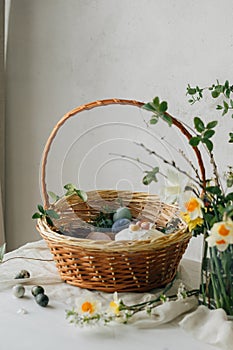 Happy Easter! Stylish easter basket with natural dyed eggs, meat, bread, butter, beets and spring flowers on rustic table.