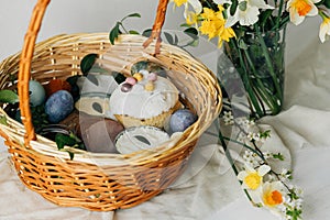 Happy Easter! Stylish easter basket with natural dyed eggs, meat, bread, butter, beets and spring flowers on rustic table.