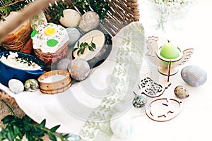 Happy Easter. Stylish Easter eggs, easter bread cake, ham, beets, sausage, butter, green branches in wicker basket on white wooden