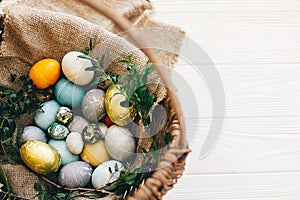 Happy Easter. Stylish easter eggs in rustic basket on white wooden background, top view. Easter hunt concept. Modern easter eggs