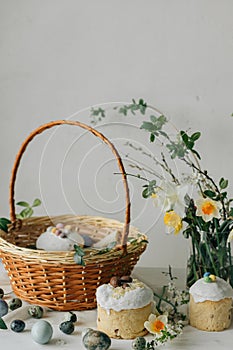 Happy Easter! Stylish easter natural dyed eggs, bread, basket with food and spring flowers on rustic table. Traditional easter