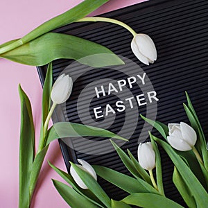 Happy Easter - text on black letter board with white tulips on pink background