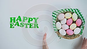 Happy Easter text, woman putting basket with colored eggs on white background