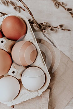 Happy Easter unpainted eggs in a cardboard box on a grey wooden table with willow branches. Rustic style