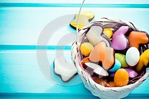 Happy Easter. White straw basket full of colorfull sweets eggs and rabbits on light blue background. Copyspace.