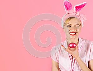 Happy Easter. Winking girl hunts for Easter eggs. Smiling woman in rabbit bunny ears with colored egg.