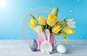 Happy Easter. Wooden decorative eggs, funny bunnie and bouquet of yellow tulips in bucket on blue background. Concept: beautiful
