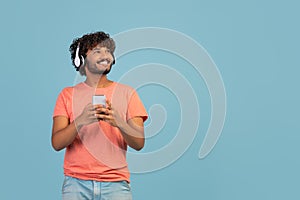 Happy eastern guy using wireless headset and smartphone, copy space