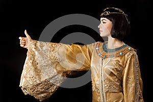 Happy Egyptian woman like Cleopatra with thumbs up gesture, on black background
