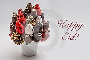 Happy Eid greeting card with red lettering; A bundle of edible flowers, arrangement of strawberries covered with chocolate