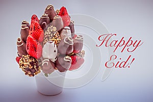 Happy Eid greeting card with red lettering; A bundle of edible flowers, arrangement of strawberries covered with chocolate