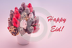 Happy Eid greeting card with red lettering; A bundle of edible flowers, arrangement of strawberries covered with chocolate