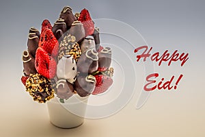 Happy Eid greeting card with red lettering; A bundle of edible flowers, arrangement of strawberries covered with chocolate