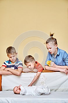 Happy elder brothers look and touch gently baby sibling