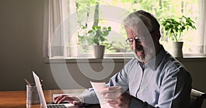 Happy elderly 60s man paying utility bills online on computer.