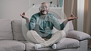 Happy elderly african american man sit on sofa in lotus position with folded fingers grandpa is meditating finds harmony