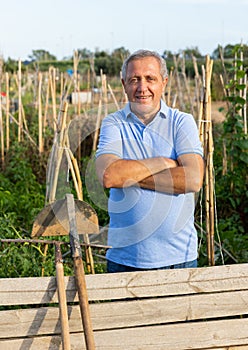 Happy elderly amateur gardener standing near wooden fence at smallholding