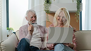 Happy elderly Caucasian family couple man woman grandparents remote paying pension credit card on Internet using laptop